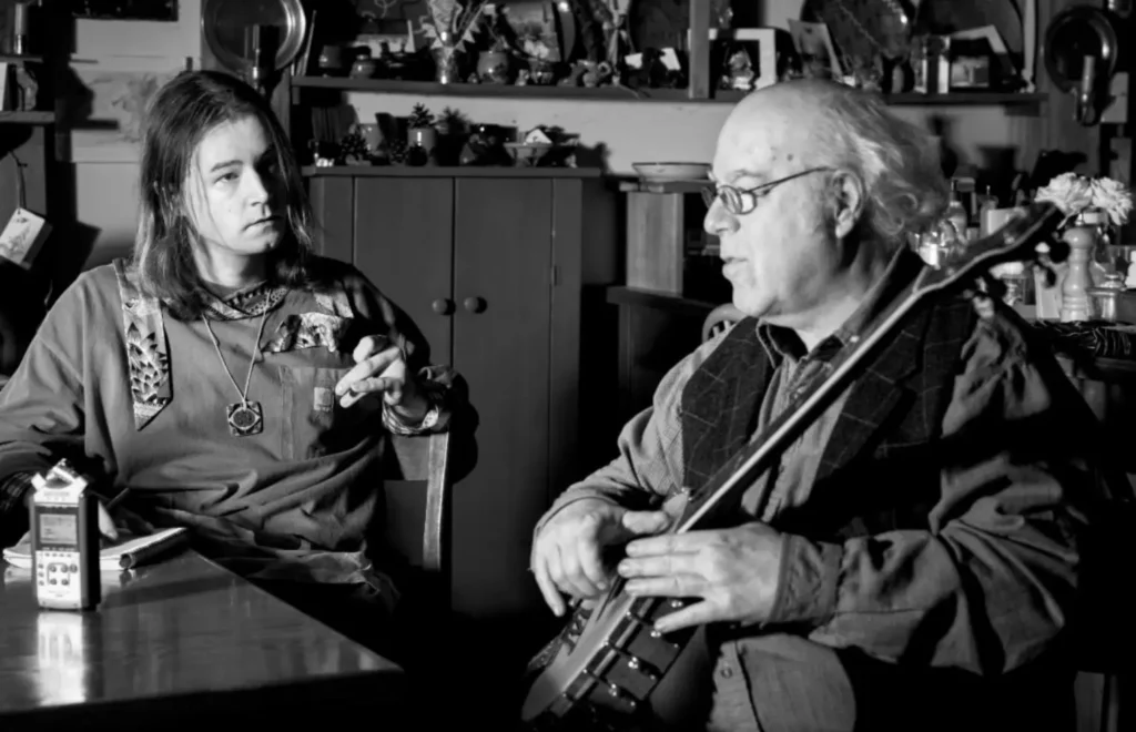 black and white photo of a young man talking to an old man with a banjo